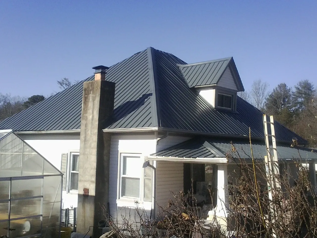 Dark blue standing seam metal roof on a white farmhouse with dormer — Slate & Tile Roof Repair by Roofing Brothers in Rochdale