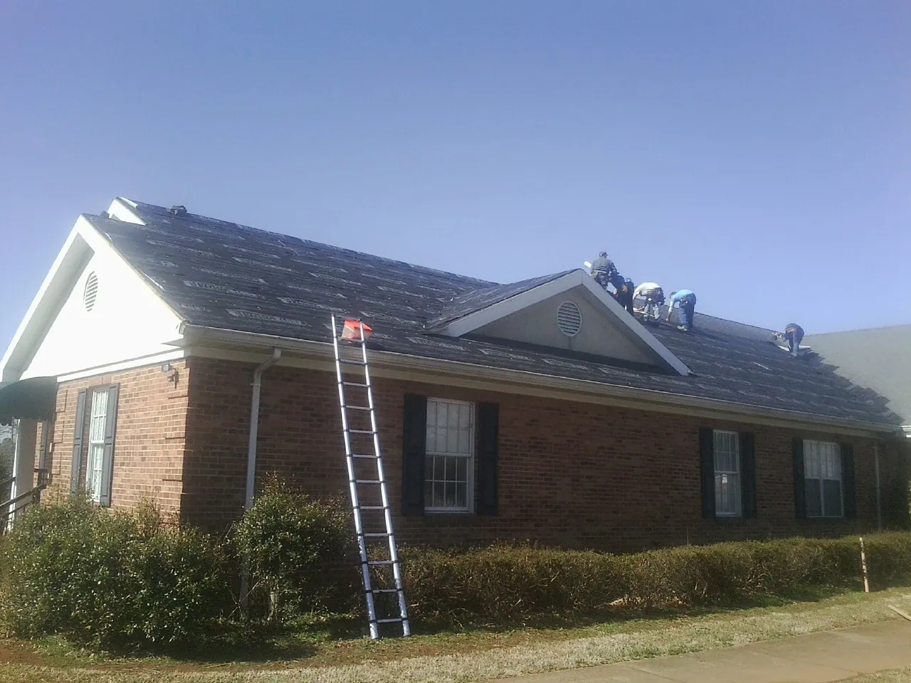 Crew tearing shingles off a brick ranch roof with a ladder set — Emergency Roof Repair work by our crew in Rochdale