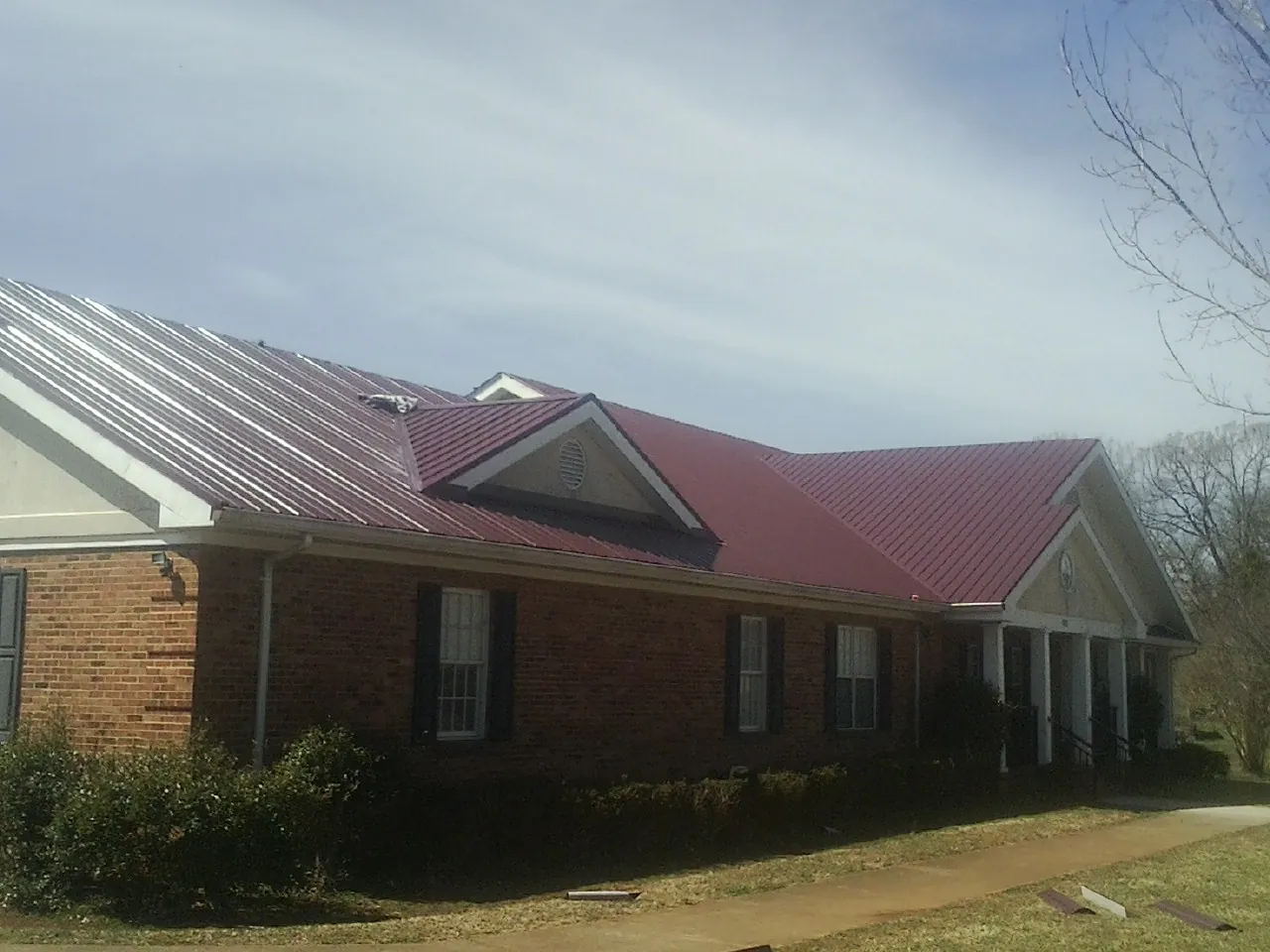Red metal roof with gabled entries on a long brick building, from a Hail Damage Roof Repair job in Rochdale