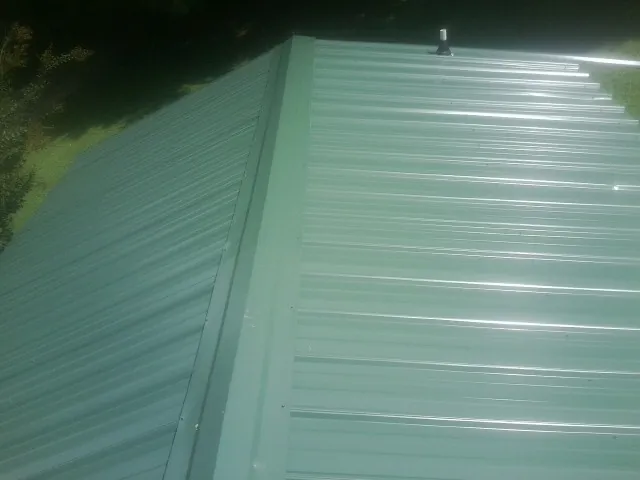 New green metal panels meeting at the ridge of a roof — Flat Roof Repair work by our crew in Rochdale