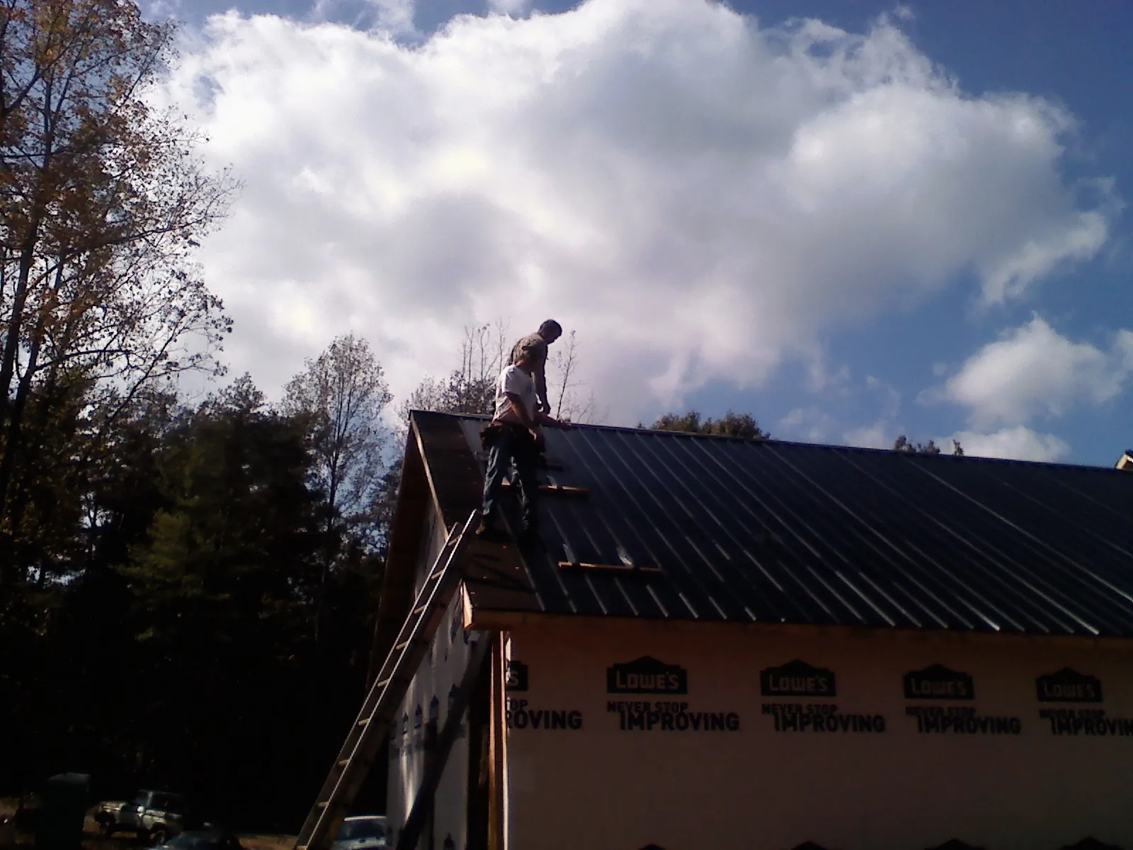 Roofer fastening dark metal panels high against a cloudy sky, from a Roof Inspection job in Rochdale