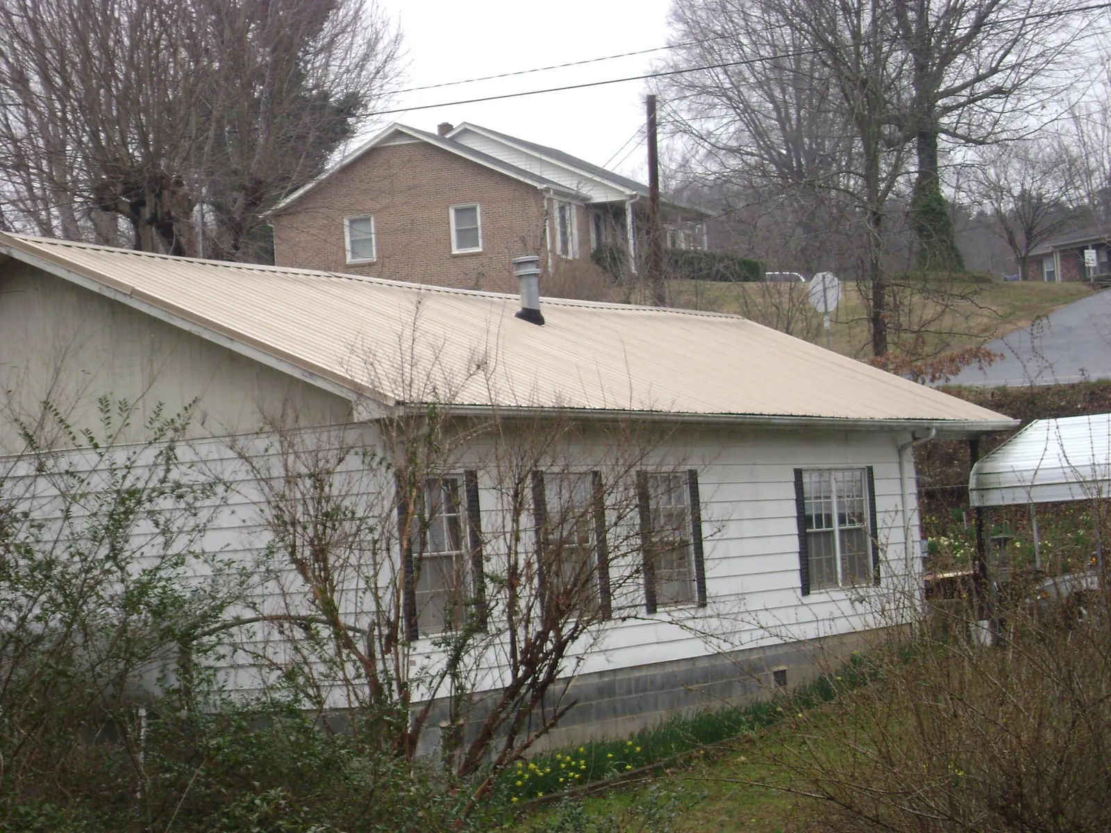 Tan metal roof on a white sided house set into a hillside — Commercial Roofing by Roofing Brothers in Rochdale