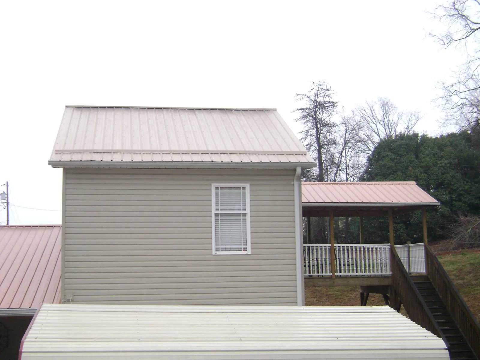 Tan metal roofs on a two story addition and attached porch, from a Roof Replacement job in Rochdale